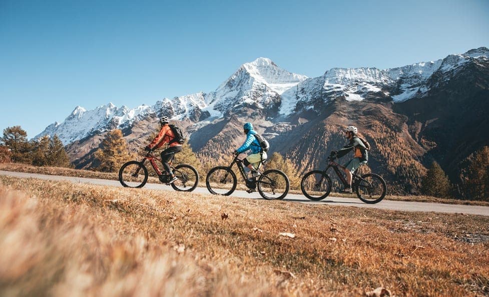 A group of riders climbing up a road with the Alps in the background