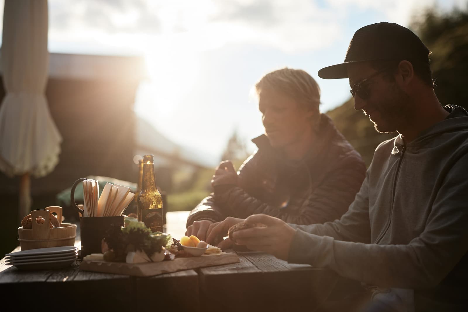 Two riders enjoying an alpine platter of cheese and dried meat outdoors.